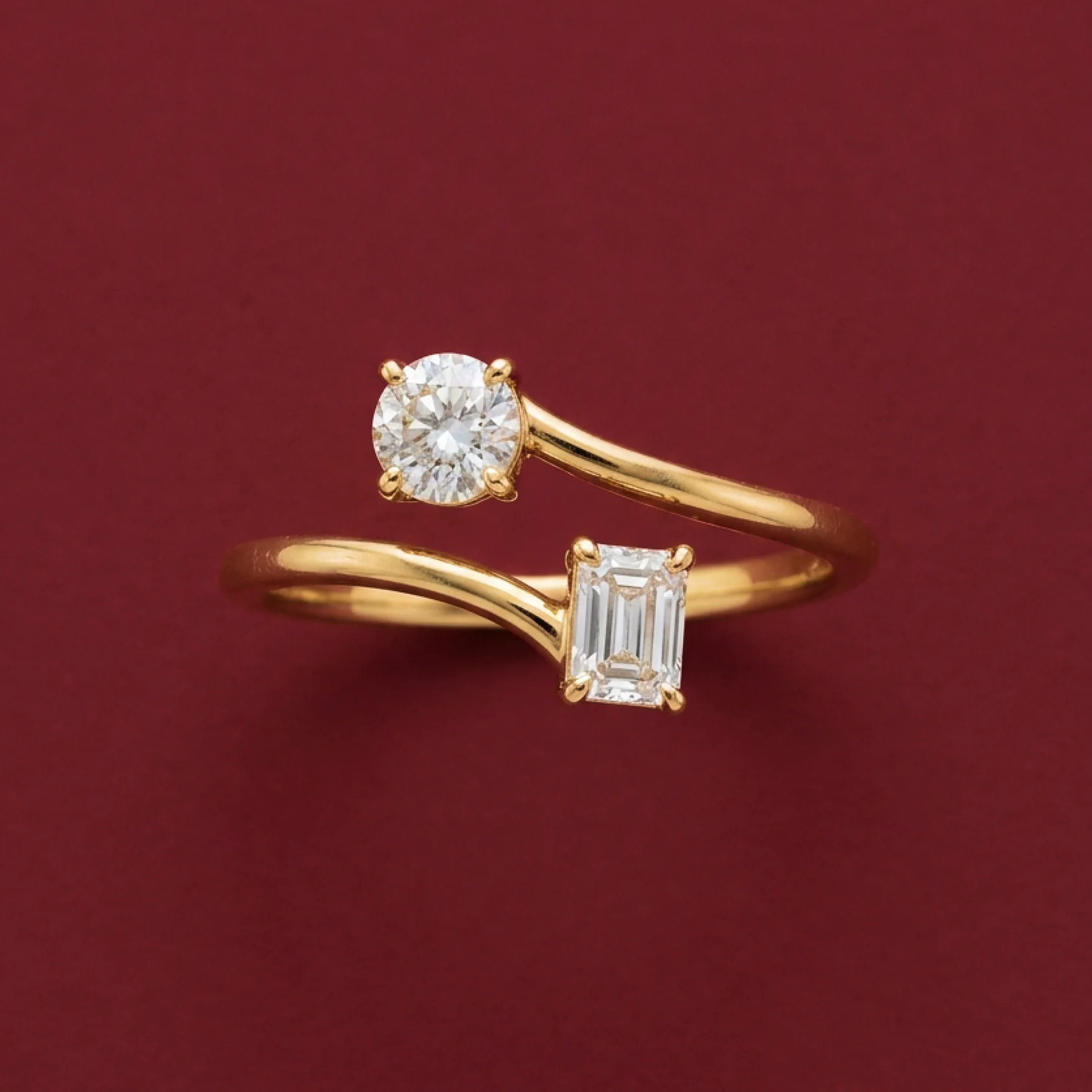 A warm-gold ring with oval and emerald-cut diamonds on burgundy velvet.