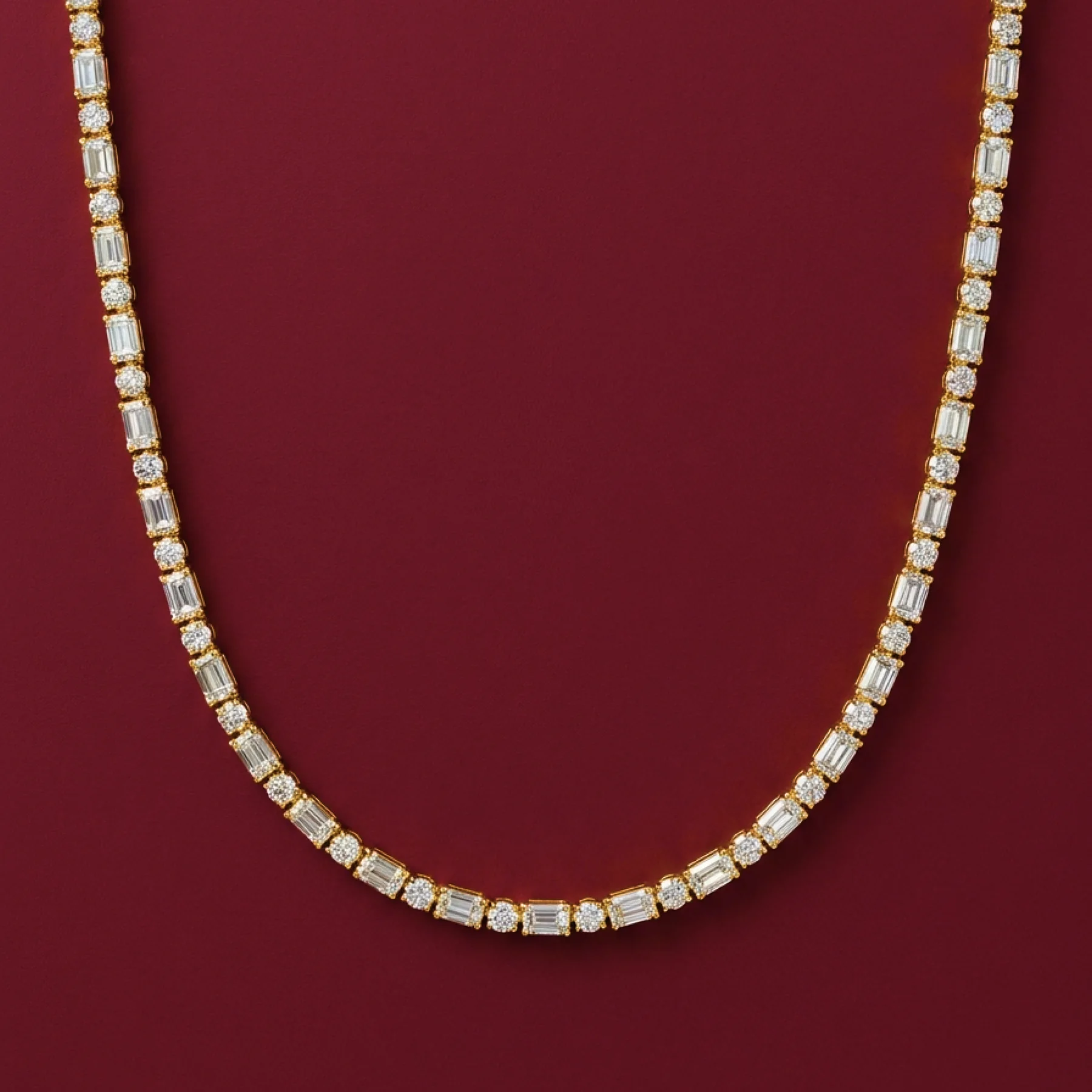 A warm-gold diamond tennis necklace on burgundy velvet.