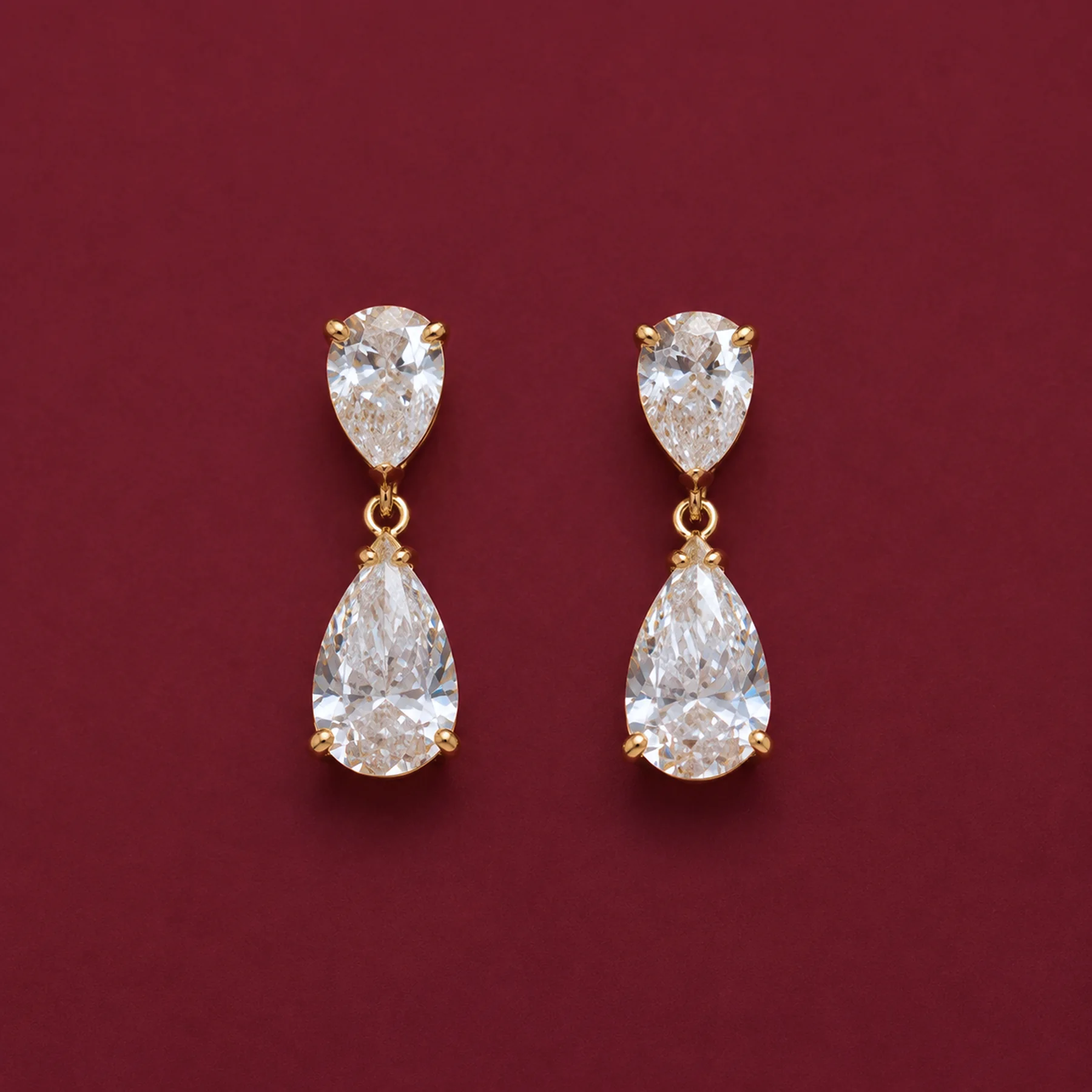 A pair of warm-gold pear diamond drop earrings on burgundy velvet.