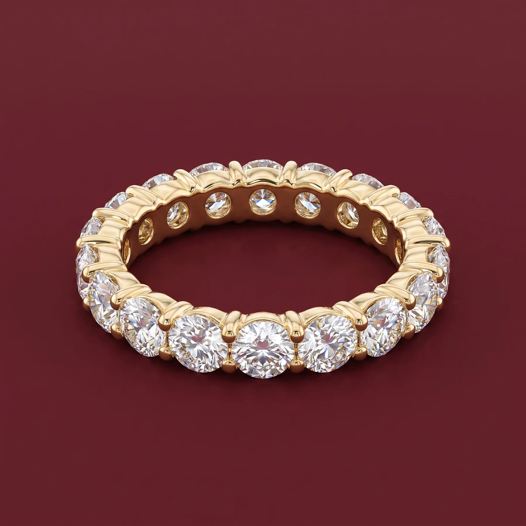 A warm-gold eternity ring with round diamonds on burgundy velvet.
