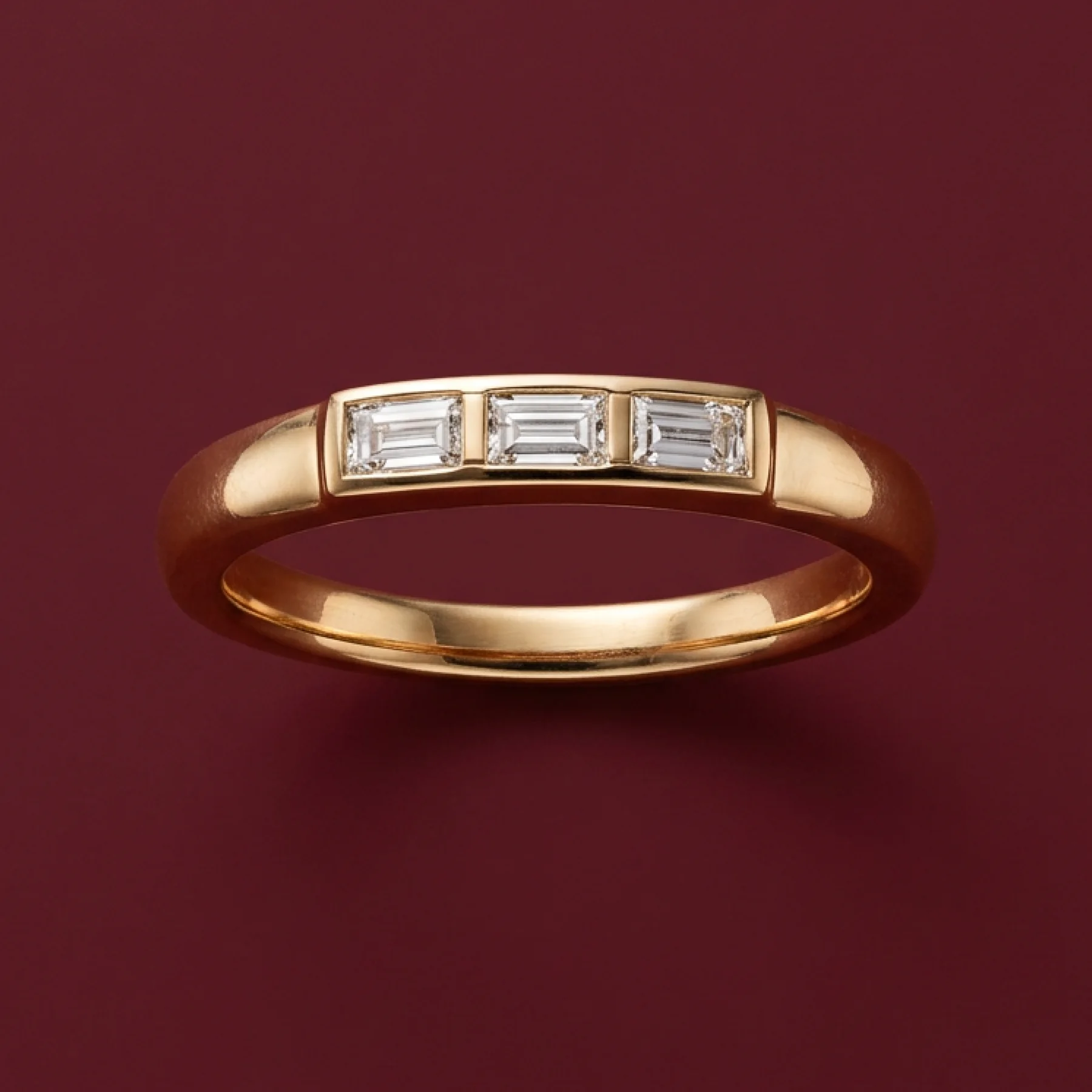 A warm-gold family ring with a baguette diamond on burgundy velvet.