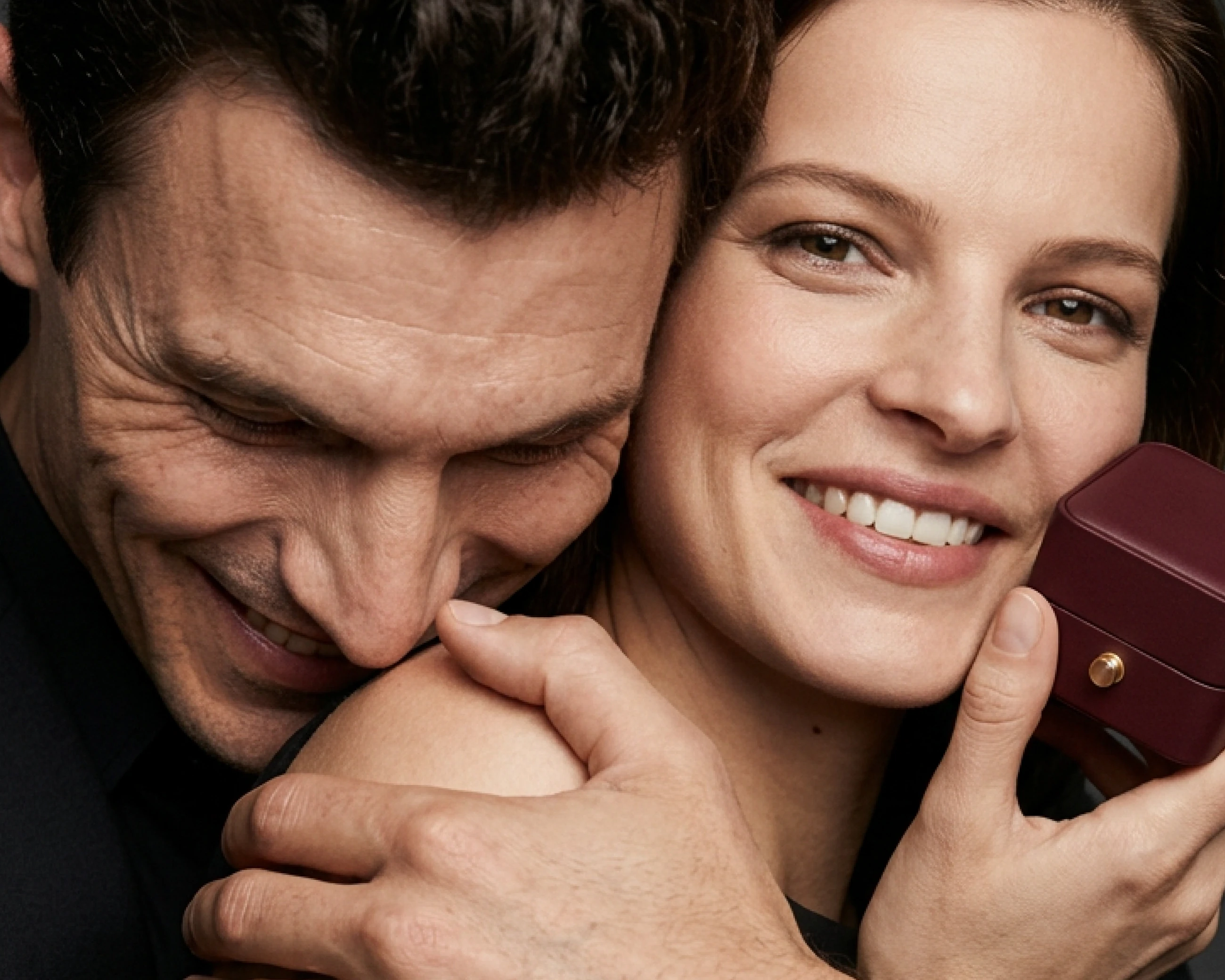 A couple hold close beside a burgundy Maison jewellery box.
